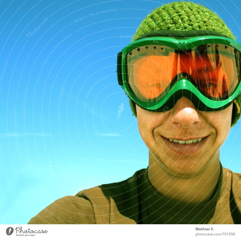 Smile like you mean it Skiing goggles Young man Grinning Cap Snowboarder Man Blue sky Green Portrait photograph Happiness Recklessness Youth (Young adults) Sky