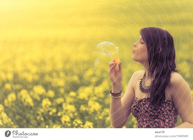Beautiful young woman with soap bubble in summer on yellow meadow from rape to horizon. Pretty girl with zest for life enjoys the sunshine break and life. Rest and recharge energy from time stress in the environment and nature idyll.