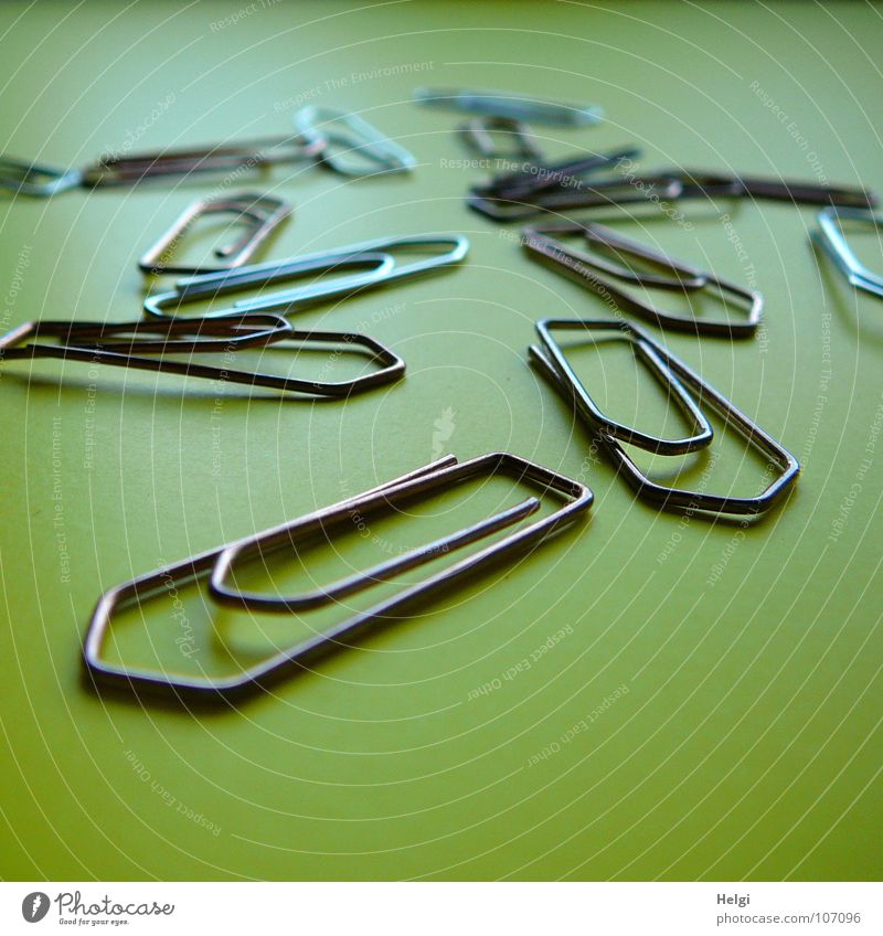 several paperclips are lying on a yellow background Holder Paper clip Tack Small Wire Curved Yellow Green Multiple Side by side Behind one another