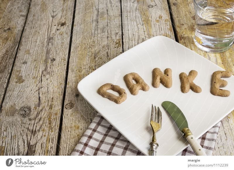 The letters THANKS on a plate with napkin, knife, fork and a water glass on a rustic wooden table Food Breakfast Lunch Dinner Beverage Cold drink Drinking water