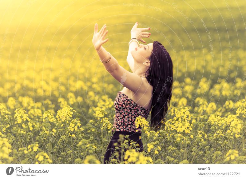 Beautiful young woman in summer on yellow meadow from rape to horizon. Pretty girl with zest for life enjoys the sunshine break and life. Rest and recharge energy from time stress in the environment and nature idyll. Hands up, eyes closed.