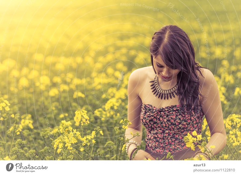 Thoughtful young woman with bowed head on yellow meadow. Attractive girl with bowed head on a meadow of flowers in yellow to the horizon in the sunshine in spring or summer. Photo of a series.
