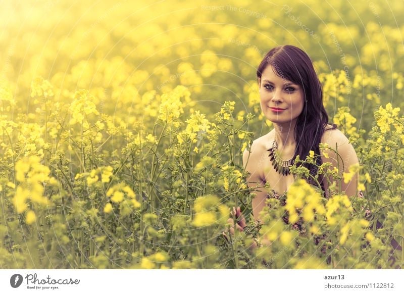 Happy summer love woman sitting smiling in canola field. Attractive young beauty girl enjoying the warm sunny sun in nature, taking time to feel sustainability, reflection and youthful well-being.