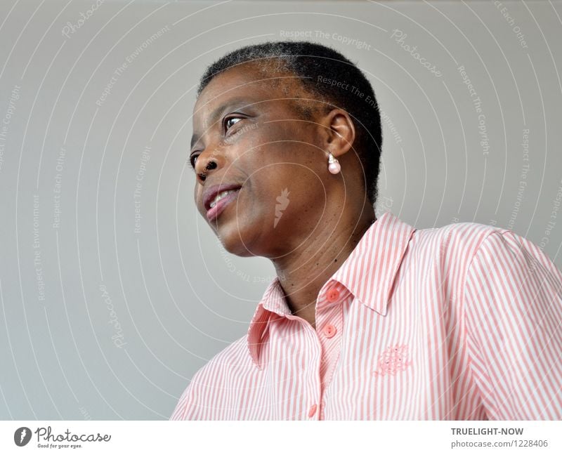 Beautiful African woman from Togo with very short hair, slightly opened mouth, one earring with pearl in a white and pink striped fine shirt with collar from below in half profile