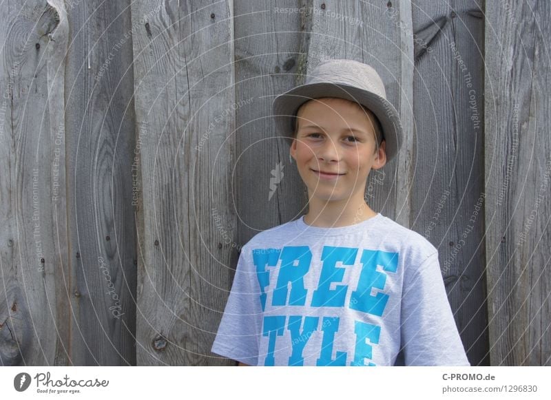 Boy with hat for wooden fence Human being Masculine Child 1 3 - 8 years Infancy 8 - 13 years Wall (barrier) Wall (building) T-shirt Hat smile Laughter Free