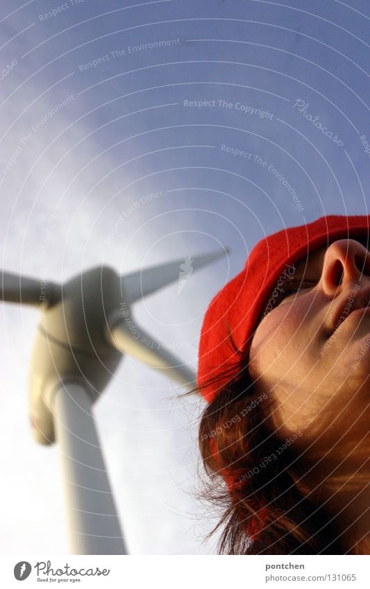 A woman with a red cap stands in front of a wind turbine. Climate change. Alternative power generation. Renewable energy Hair and hairstyles Industry