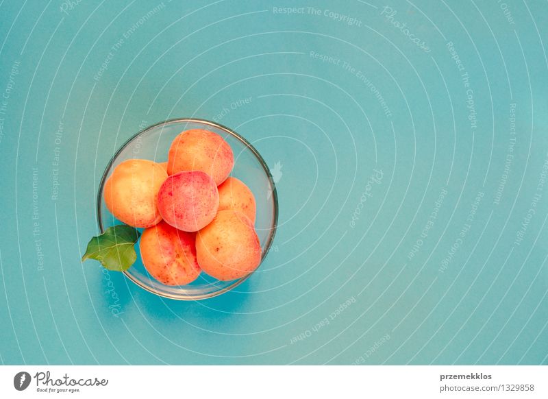 Apricots in bowl on blue background Food Fruit Organic produce Bowl Summer Nature Fresh Delicious Sweet Blue Yellow Orange glassware healthy Horizontal pit