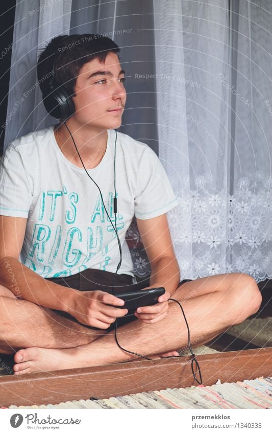 Portrait of relaxed young boy sitting at the patio door and listening to music from mobile phone Lifestyle Joy Relaxation Leisure and hobbies Summer Music