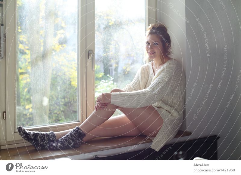 Young woman sitting on windowsill in sunlit kitchen smiling at camera Life Harmonious Well-being Youth (Young adults) Face Legs 18 - 30 years Adults Wool socks