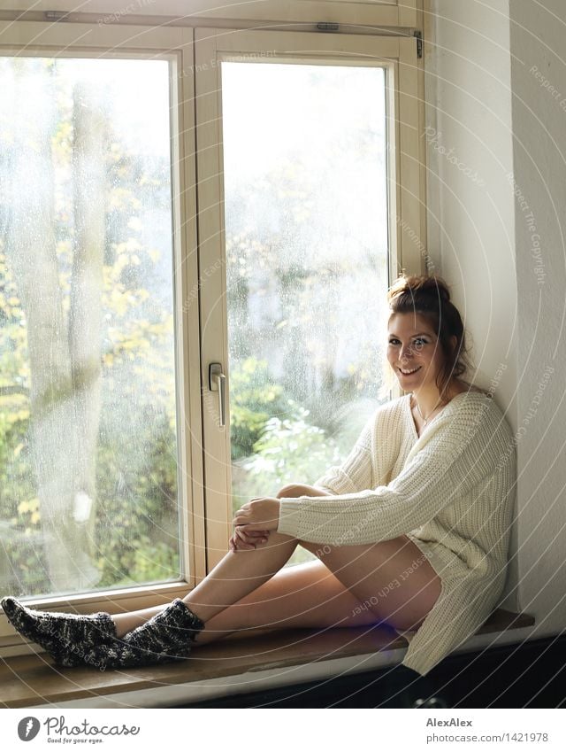 Young woman sitting in windowsill in sunlit kitchen smiling at camera Wellness Well-being Relaxation Kitchen Window Window board Youth (Young adults) Face Legs