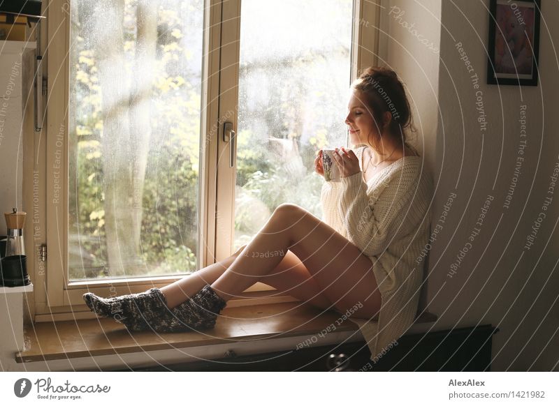 Young woman sitting in sunny kitchen in window frame enjoying coffee or tea from big cupSunday coffee Drinking Coffee Cup Mug Harmonious Relaxation