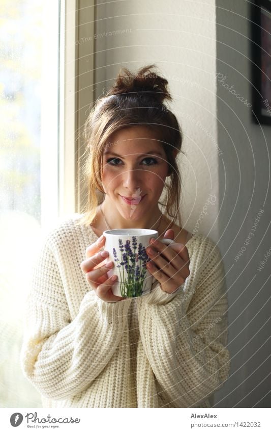 Young woman holding cup in both hands containing Sunday coffee in front of window frame in kitchen, she smiles at camera Coffee Breakfast Drinking Hot drink Cup