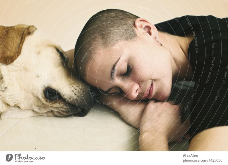 Young woman with very short hair lies resting with closed eyes head to head  with young blonde Labrador - a Royalty Free Stock Photo from Photocase
