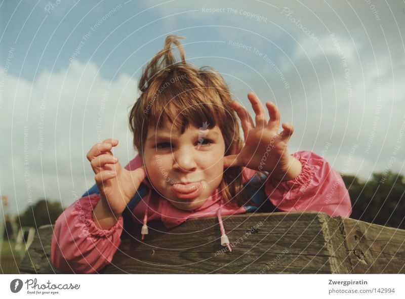 childhood Child Small Brash Grimace Girl Tongue Stick out Rain jacket Pink Blue Playground Sky Clouds Gray Closed White Wood Brown Arrangement Texture of wood