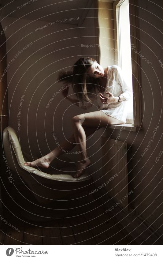 young woman sits barefoot in a window frame and runs through her long brunette hair pretty Senses Relaxation Armchair Room Young woman Youth (Young adults)
