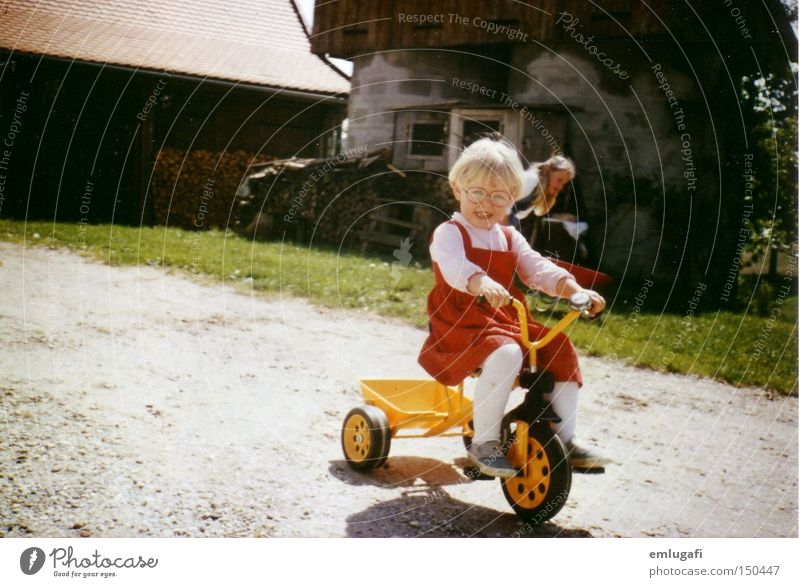 Wheels keep on turning... Yellow Red Tricycle Child Blonde Driving Farm Courtyard Eyeglasses Dress Joy Toddler Summer