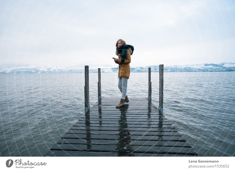 Young woman with smartphone on a wintry jetty Cellphone PDA Landscape Water Sky Winter Fog Snow Mountain Lake Switzerland Europe Small Town Footbridge Coat