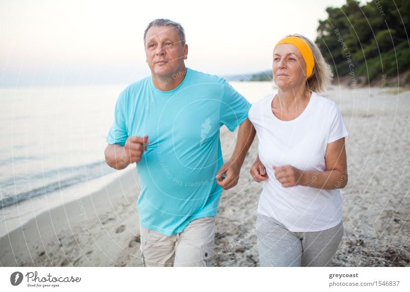 Senior man and woman having a run along the shore. Scene with sea, sand and trees. Healthy and active way of life Lifestyle Leisure and hobbies