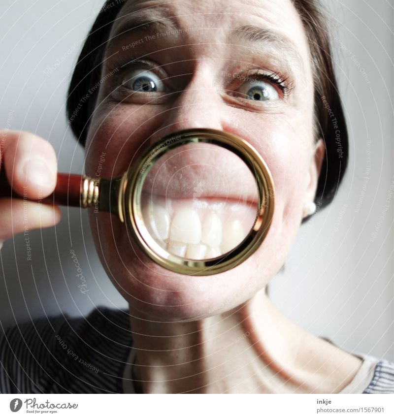 Grinning woman shows her white teeth through a magnifying glass Joy Woman Adults Life Face Teeth 1 Human being 30 - 45 years Magnifying glass Smiling Funny Near