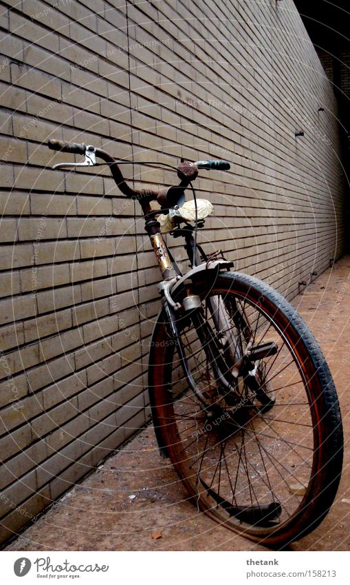 An old bicycle with flat tires leans against a brick wall in a factory building. Calm Bicycle Rust Brick Old Broken Loneliness Past Transience Scrap metal