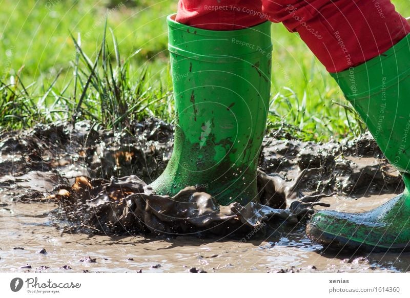 Green rubber boots splashing in muddy puddle Rubber boots Puddle Mud slush Playing Child Feet Human being Water Drops of water Meadow Jump Dirty Wet Brown Red