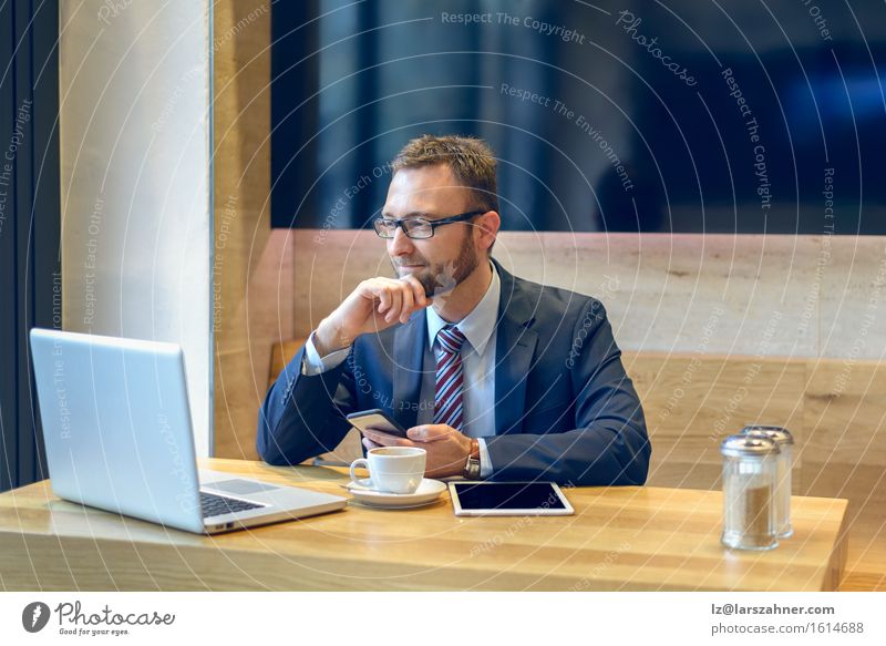 Businessman enjoying coffee and checking his mobile phone for messages with a smile with his laptop and tablet open on the table Coffee Face Work and employment