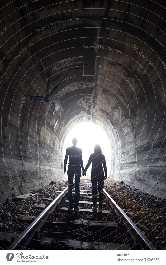 Couple walking together through a railway tunnel couple adventure arched asylum bright concept danger dark emigrants fugitive hidden holding hands hope