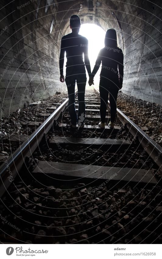Couple walking together through a railway tunnel couple adventure arched asylum bright concept danger dark emigrants fugitive hidden holding hands hope