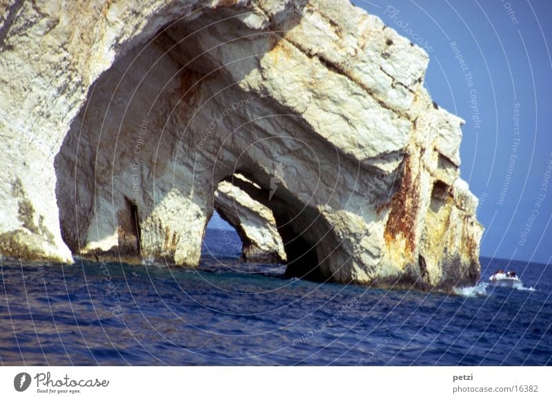 Caves in the Ionian Sea Ocean Water Cloudless sky Sun Summer Rock Waves Mediterranean sea Watercraft Blue Gray Vista Opposites: solid rock agitated water