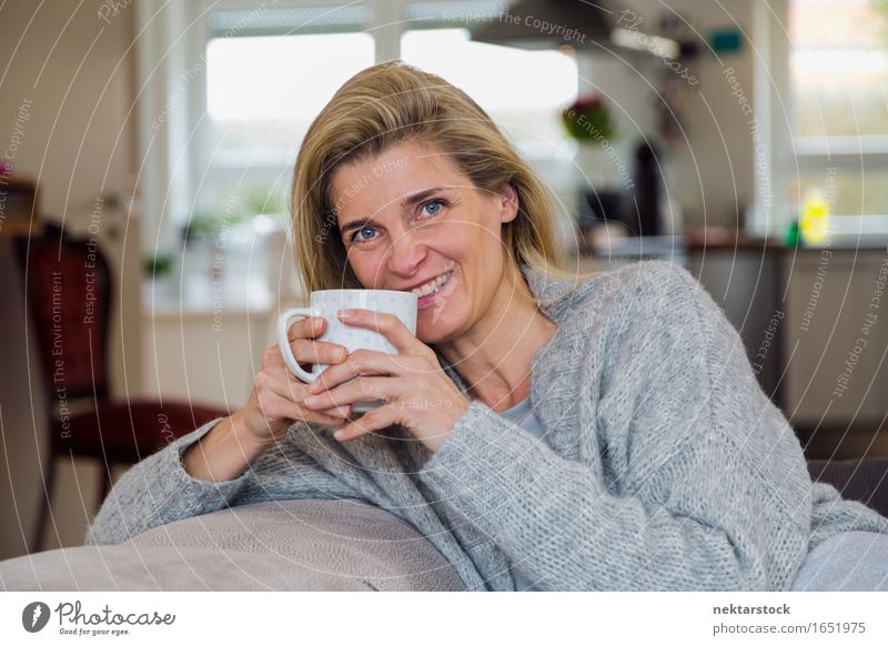 Attractive blonde woman relaxing at home Beverage Coffee Lifestyle Joy Happy Contentment Relaxation Leisure and hobbies Sofa Woman Adults Smiling Friendliness
