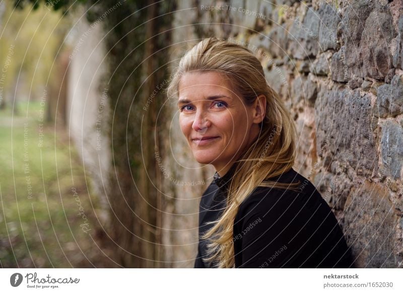 portrait of woman leaning against a wall in park Lifestyle Happy Contentment Calm Human being Woman Adults Blonde Stone Smiling Friendliness Natural