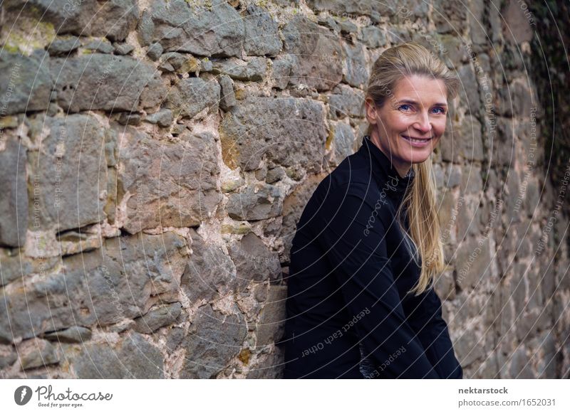 portrait of woman leaning against wall in park Lifestyle Happy Contentment Calm Human being Woman Adults Blonde Stone Smiling Friendliness Natural