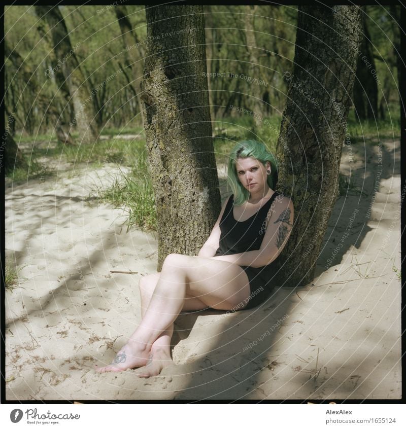 young woman with turquoise hair sits barefoot leaning against tree in beach forest and looks at camera Relaxation Vacation & Travel Trip Summer vacation