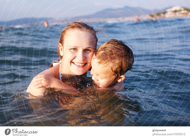Happy attractive young mother with a beautiful smile teaching her young son to swim as they float together in the sea Joy Relaxation Playing Summer Beach Ocean