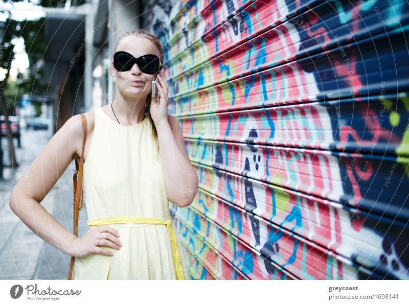 Woman in sunglasses chatting on a mobile phone while standing alongside a wall covered in colourful graffiti or a mural Lifestyle Style Happy Beautiful