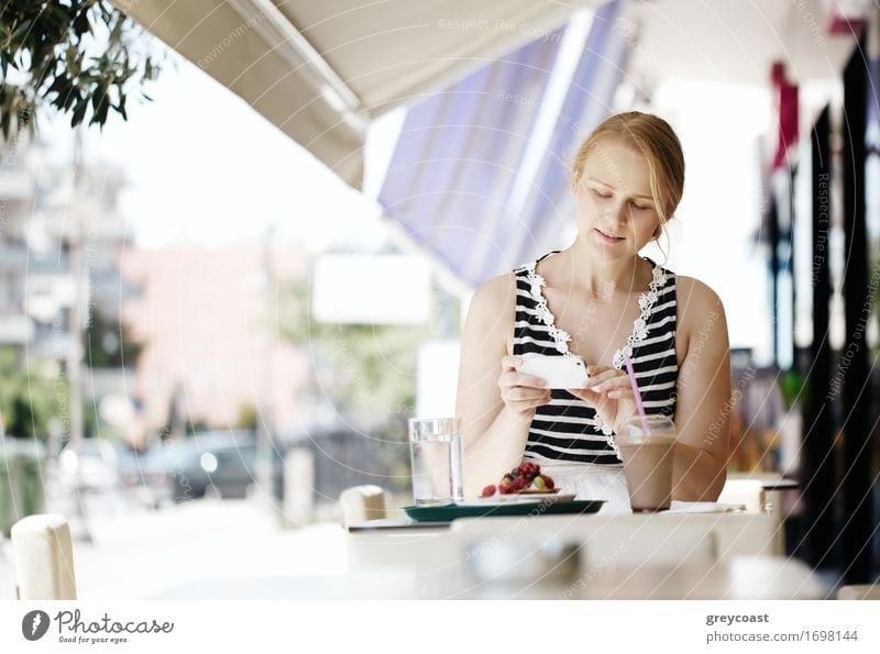 Attractive woman taking picture of a pastry on her smart phone as she sits at a table at an open-air restaurant enjoying refreshments Fruit Eating Breakfast