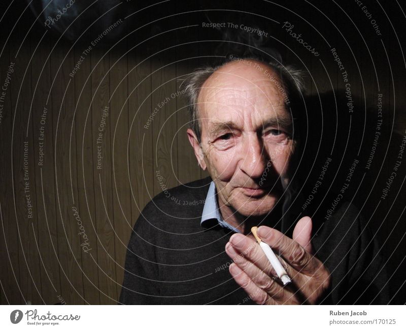 Grandfather smokes. Colour photo Interior shot Copy Space left Neutral Background Shadow Contrast Portrait photograph Looking into the camera Forward Smoking