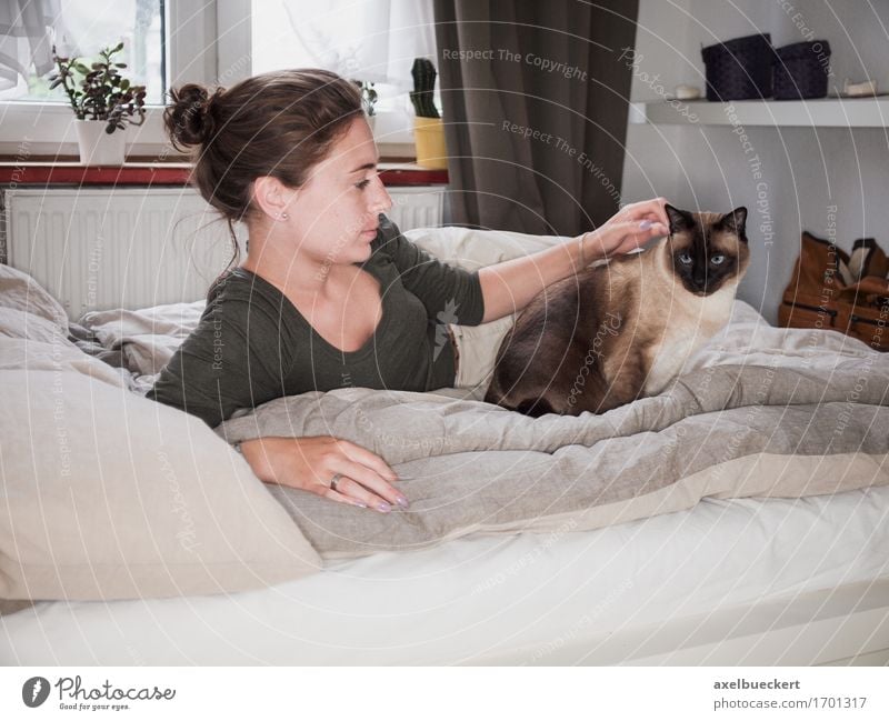 young woman lies with Siamese cat on her bed Lifestyle Leisure and hobbies Flat (apartment) Bed Bedroom Human being Feminine Young woman Youth (Young adults)