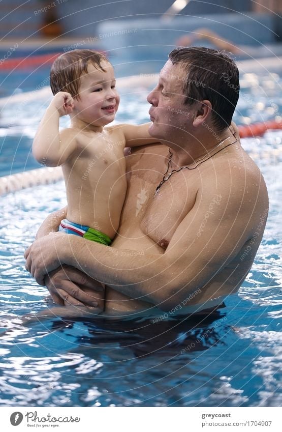 Grandfather playing with his little grandson in a swimming pool holding him above the water in his arms as they smile at each other sharing a tender moment Joy