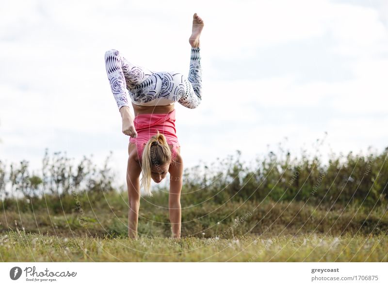 Agile young woman doing a handstand outdoors in the countryside balancing on her hands with her legs bent in opposite directions Sports Girl Young woman