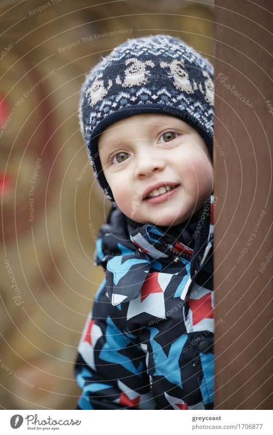 Cute little boy in a warm jacket and knitted winter cap peering around a door at the camera with a lovely friendly smile Beautiful Winter Child Baby Toddler