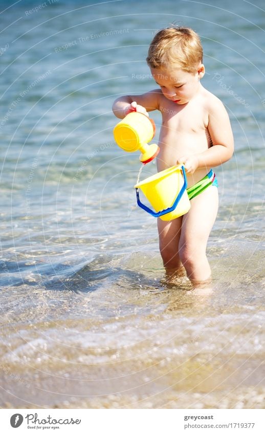 Adorable little boy playing in the sea enjoying the summer sunshine as he paddles in the water carrying his plastic toys Lifestyle Joy Happy Beautiful