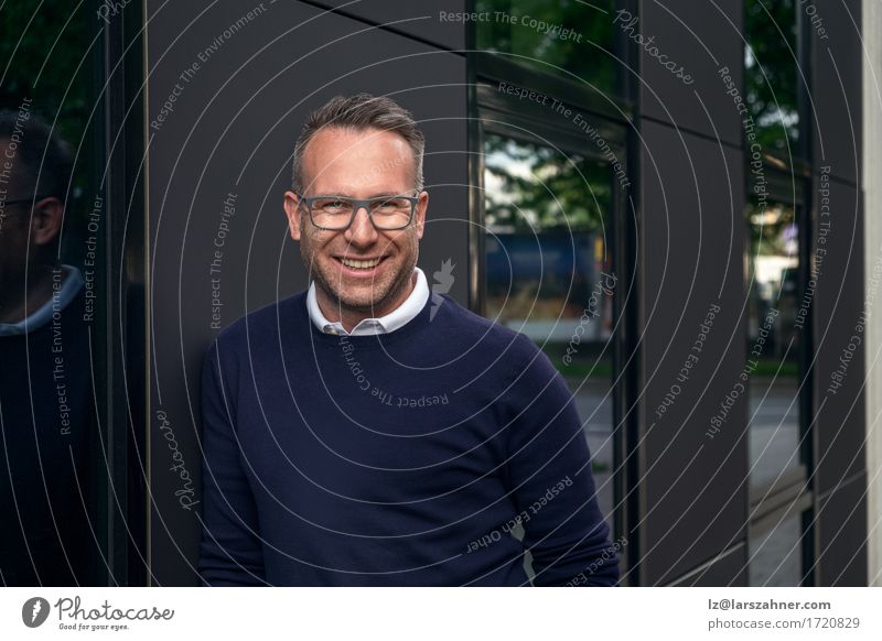Handsome smiling middle aged man wearing eyeglasses and sweater leaning against building outside with trees reflecting in window Happy Face Business Masculine