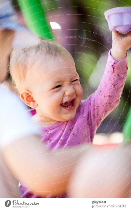 Adorable happy laughing little baby playing with a toy as it sits on its mothers lap, candid portrait over the mothers shoulder Joy Happy Playing Summer Child