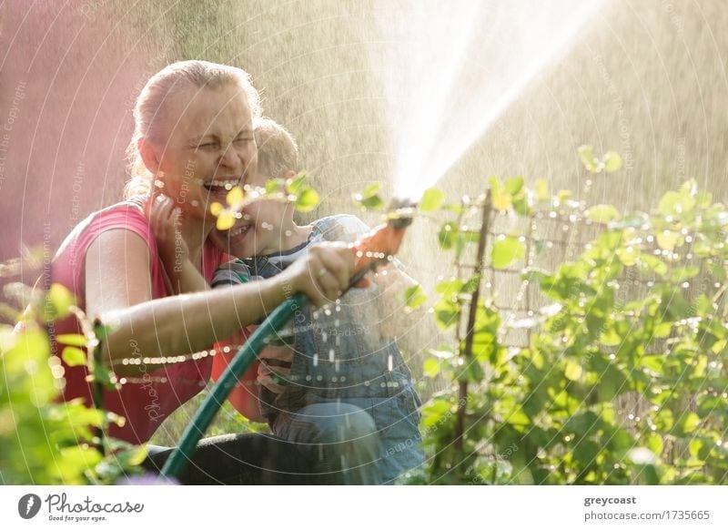 Laughing mother and son playing with a sprinkler in the garden directing the spray into the air so that it falls back wetting them Joy Happy Playing Summer