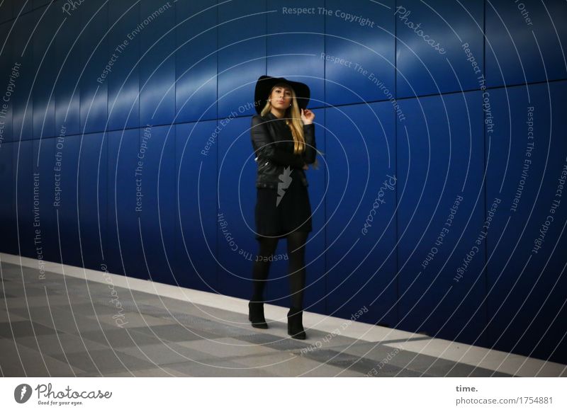 Woman with hat in front of blue wall Feminine Adults 1 Human being Wall (barrier) Wall (building) Lanes & trails Tunnel Station hall Coat Boots Hat Blonde