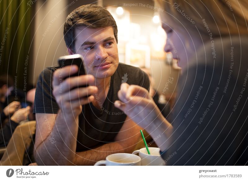 Young man using cellphone during the meeting with a girl in a cafe, but his look is attracted by someone else Tea Meeting Telephone PDA Human being Young woman