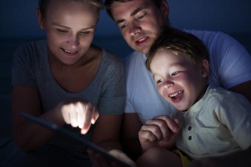 Happy family of three with pad late in the evening. Laughing child looking at screen where mother pointing at something Joy Leisure and hobbies Playing