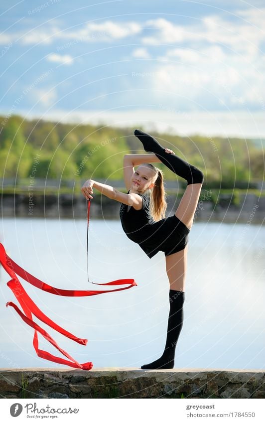 Teen rhythmic gymnast is holding leg in vertical split doing ribbon