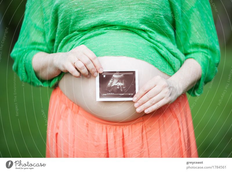 Close-up shot of a pregnant woman holding ultrasound scan in front of her bare belly. Happiness of pregnancy Medication Summer Woman Adults Mother